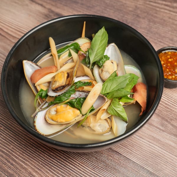 A black bowl of Luv2eat Thai Bistro's mussels in broth with basil and lemongrass, with a side of chili sauce.