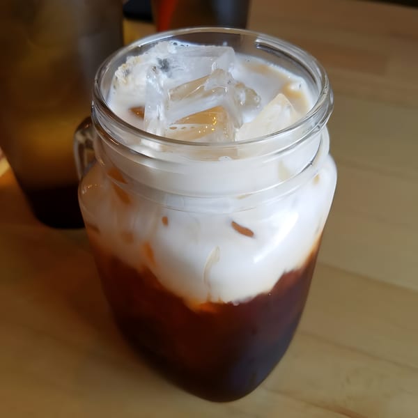 Iced Thai tea with a creamy white top layer and ice cubes in a glass mug.