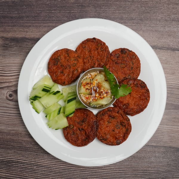 Six Luv2eat Thai Bistro fish cakes with cucumber slices and a small bowl of dipping sauce.