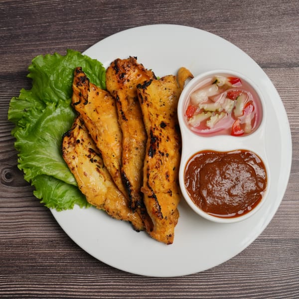 Grilled chicken satay skewers with lettuce, peanut sauce, and pickled cucumber relish on a white plate.