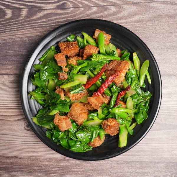Luv2eat Thai Bistro's crispy pork belly with Chinese broccoli and red chilies on a black plate.