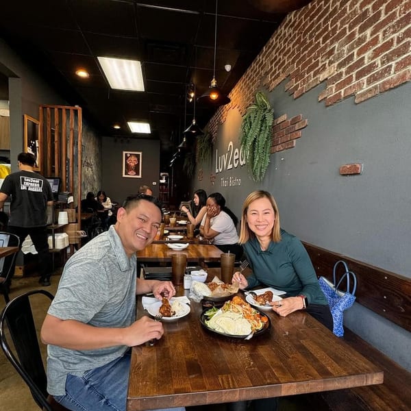 Smiling couple enjoying Thai food at a wooden table in Luv2eat Thai Bistro.