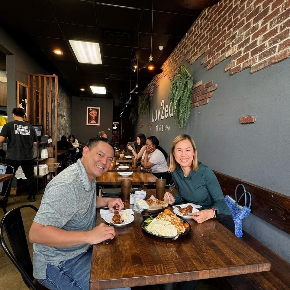 Smiling couple enjoying Thai food at a wooden table in Luv2eat Thai Bistro.