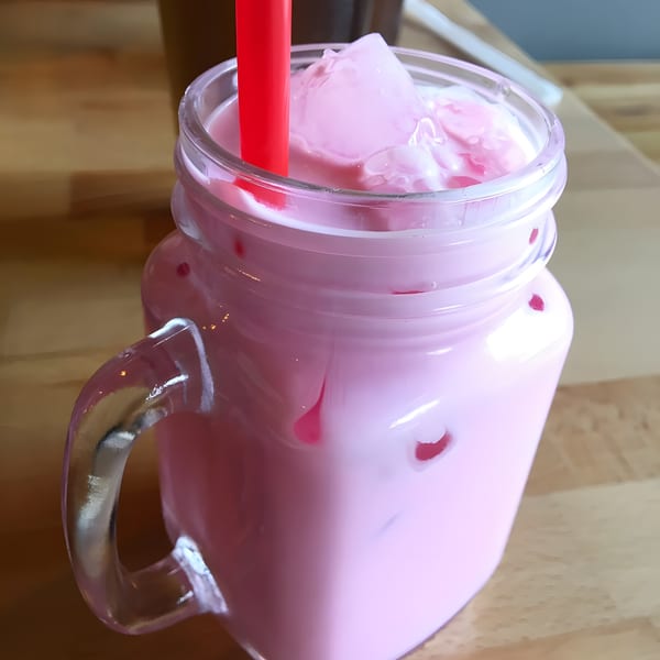 Pink Thai iced milk in a mason jar with a red straw and ice cubes.
