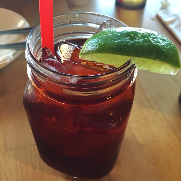 Iced Thai tea with a red straw and a lime wedge in a mason jar on a wooden table.