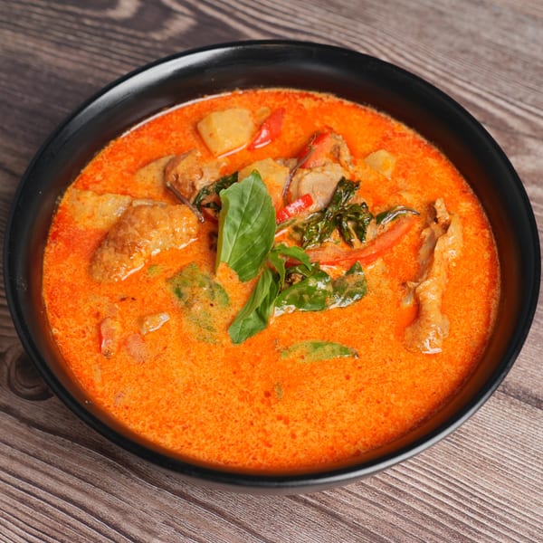 Luv2eat Thai Bistro's red curry with chicken, potatoes, and basil in a black bowl.