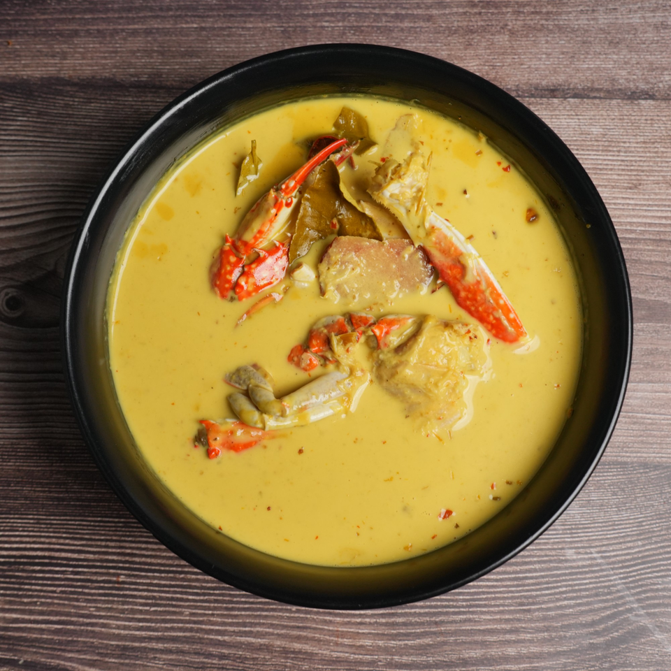 Luv2eat Thai Bistro's yellow curry with crab, kaffir lime leaves, and red chili flakes in a black bowl.